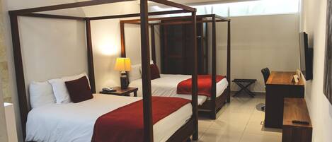 A four-poster bed with white linens and red accents, a desk with a chair, and a television on the wall.