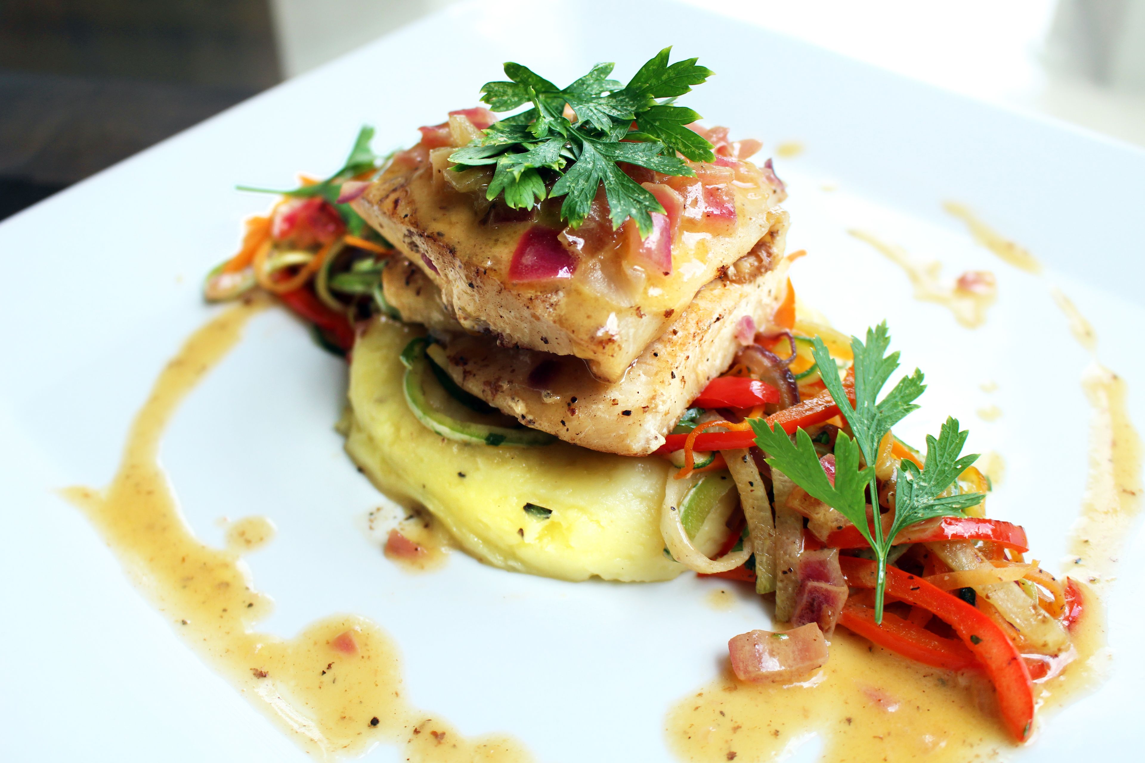 Un plat composé d’un filet de poisson, de légumes et d’une garniture, le tout présenté sur une assiette blanche.
