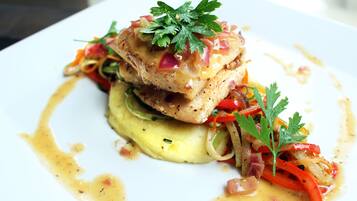Un plat composé d’un filet de poisson, de légumes et d’une garniture, le tout présenté sur une assiette blanche.