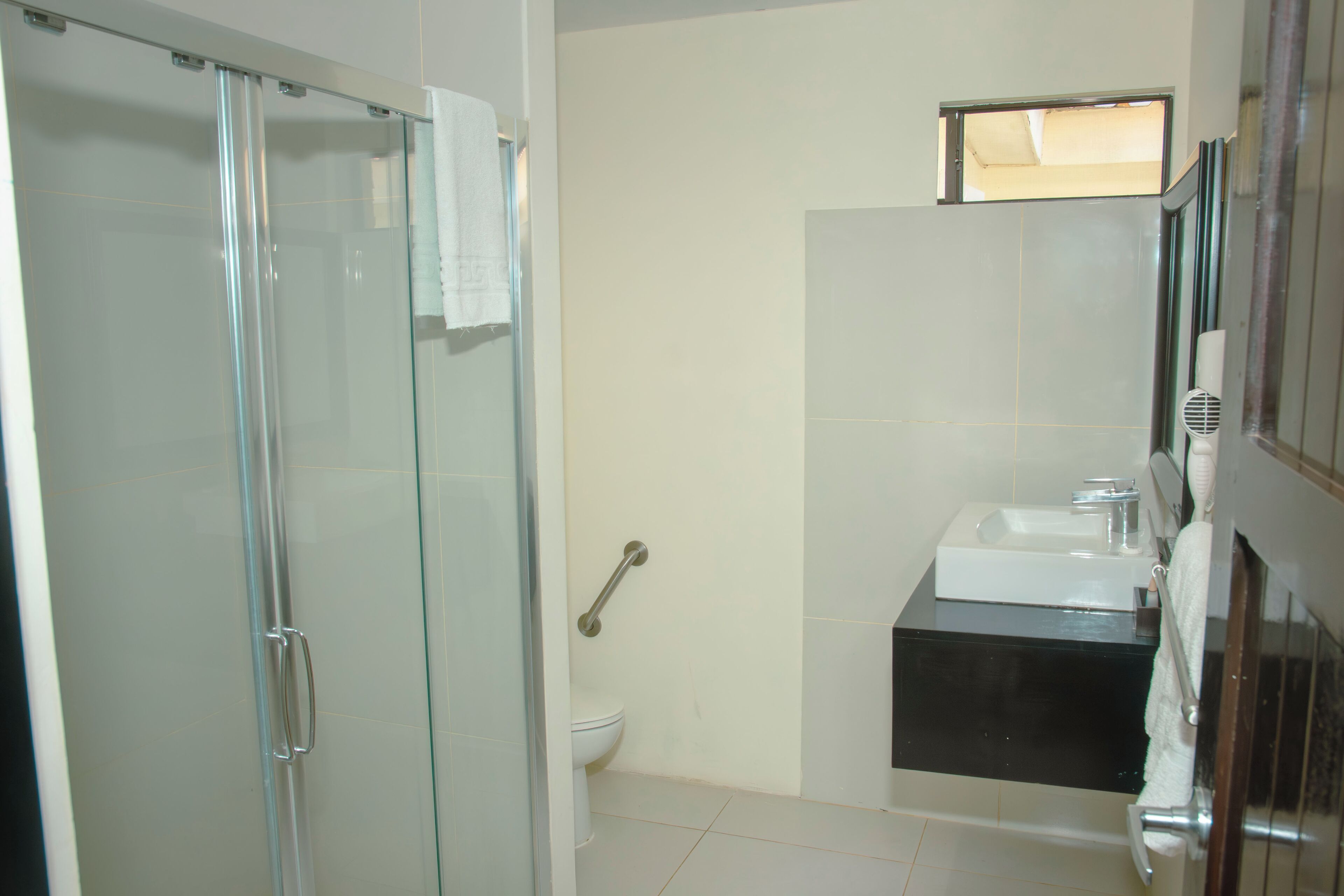 Une salle de bain avec une douche à parois de verre, des toilettes blanches, un lavabo avec un plan de toilette noir et un porte-serviettes.