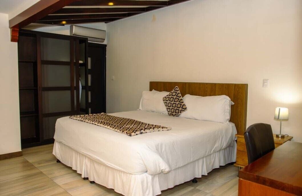 A hotel room with a large bed, a wooden headboard, a desk with a chair, and a window.