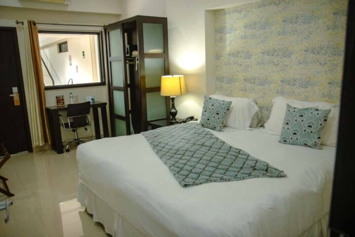 A hotel room with a bed, a desk with a chair, a lamp, and a mirror.