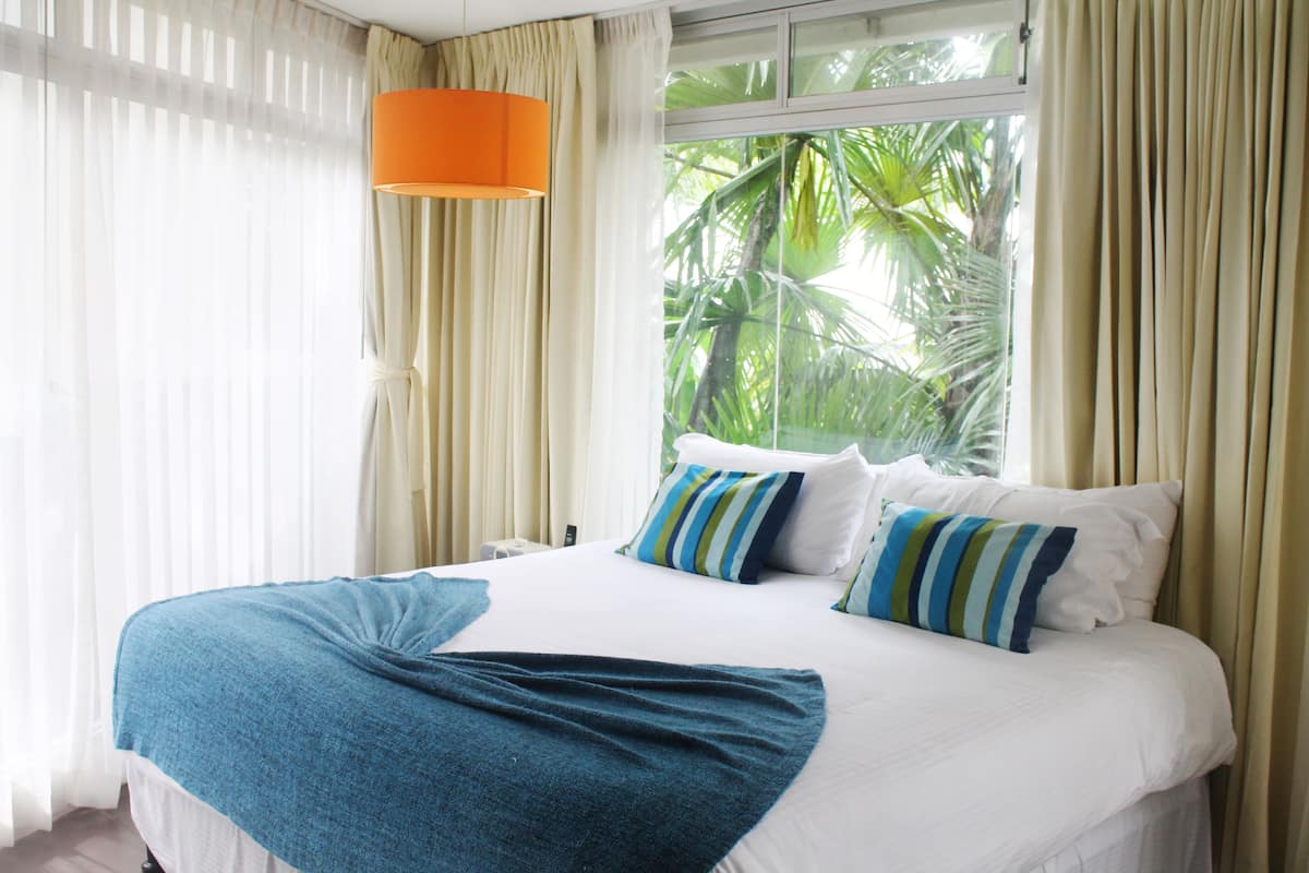 A hotel room with a large bed, a window with curtains, and a view of palm trees.