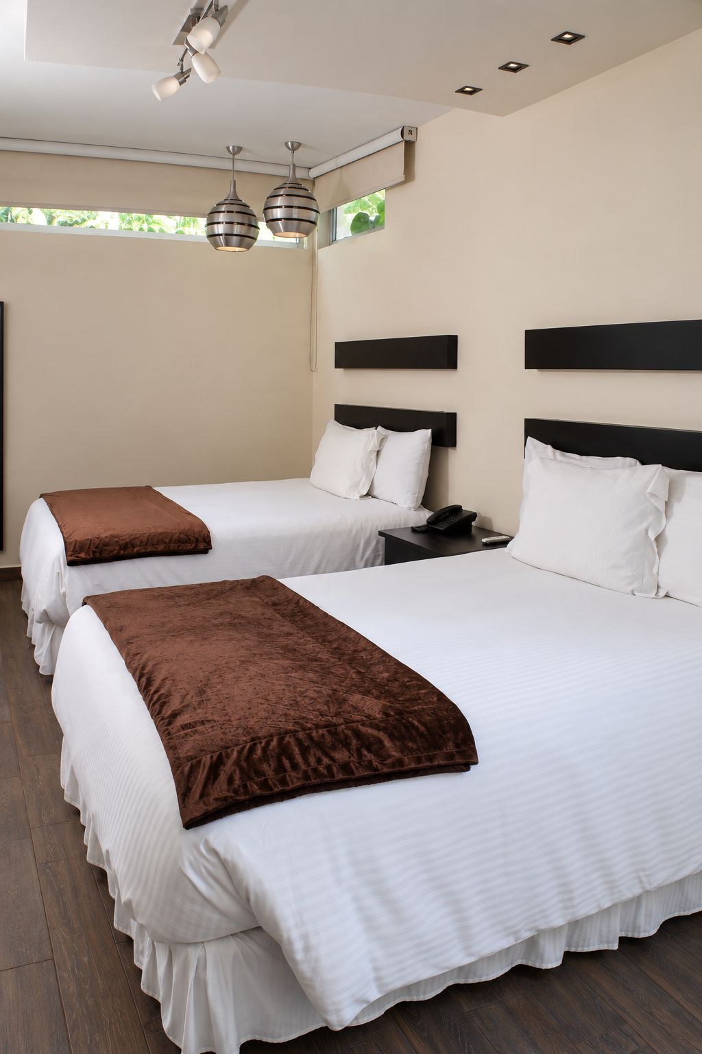 A hotel room with two beds, each with a headboard, bedside tables, and a telephone.