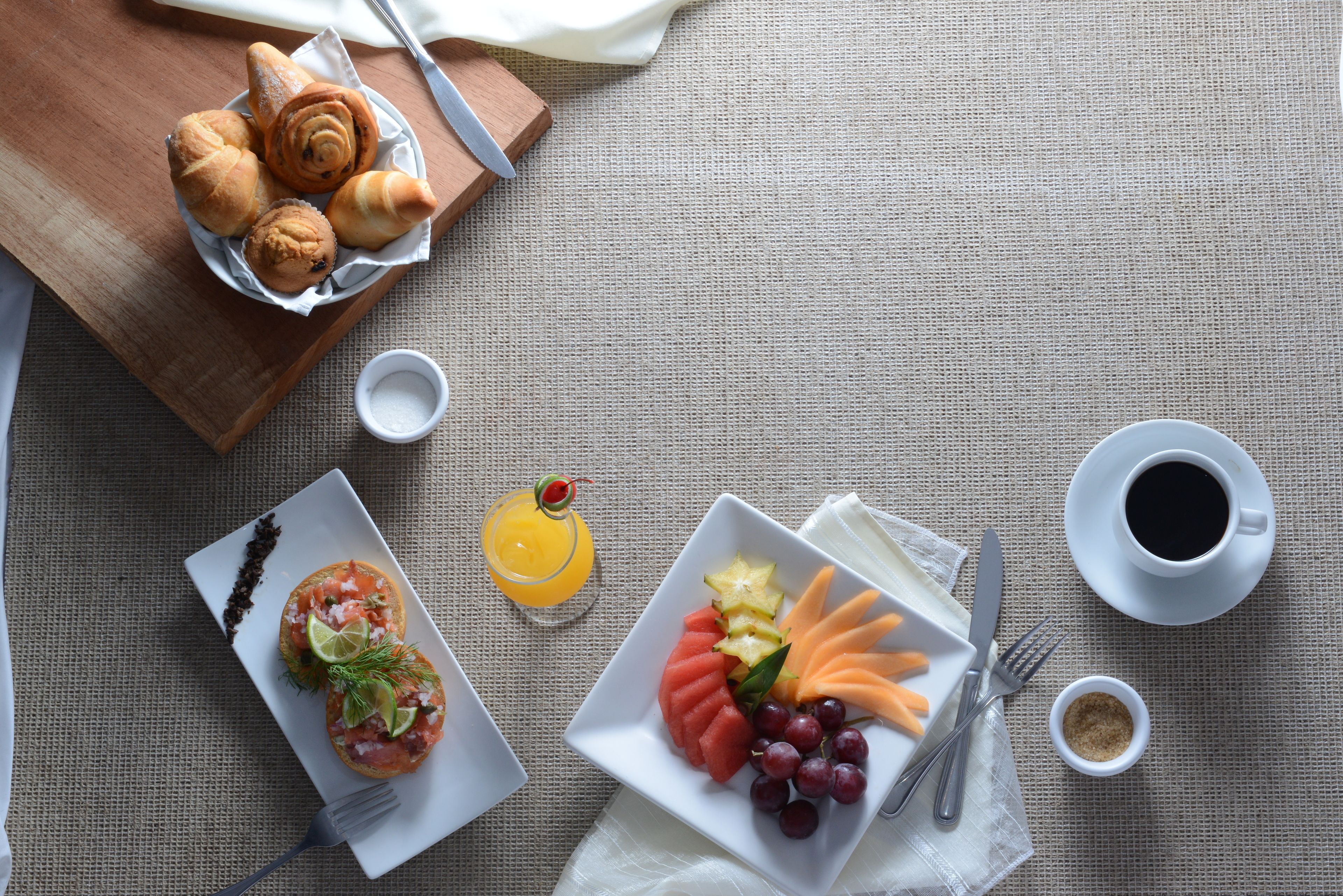 A breakfast setting with croissants, a fruit plate, a glass of orange juice, and coffee on a table.