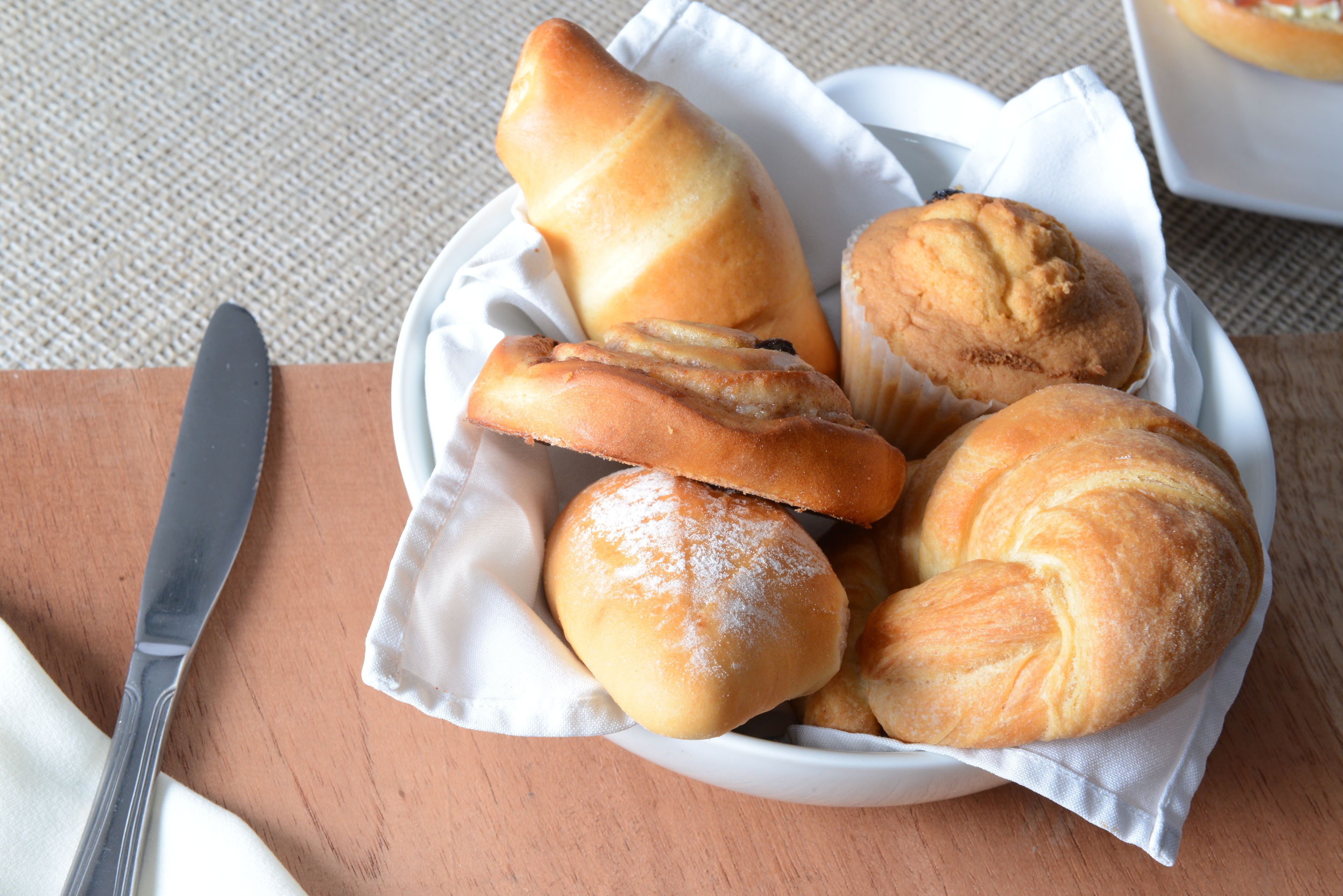 Une assiette blanche contenant différents types de pain, notamment un croissant et une baguette, posée sur une table en bois.