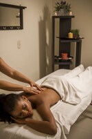 A person receiving a massage in a room with a mirror, shelf with candles, and a potted plant.