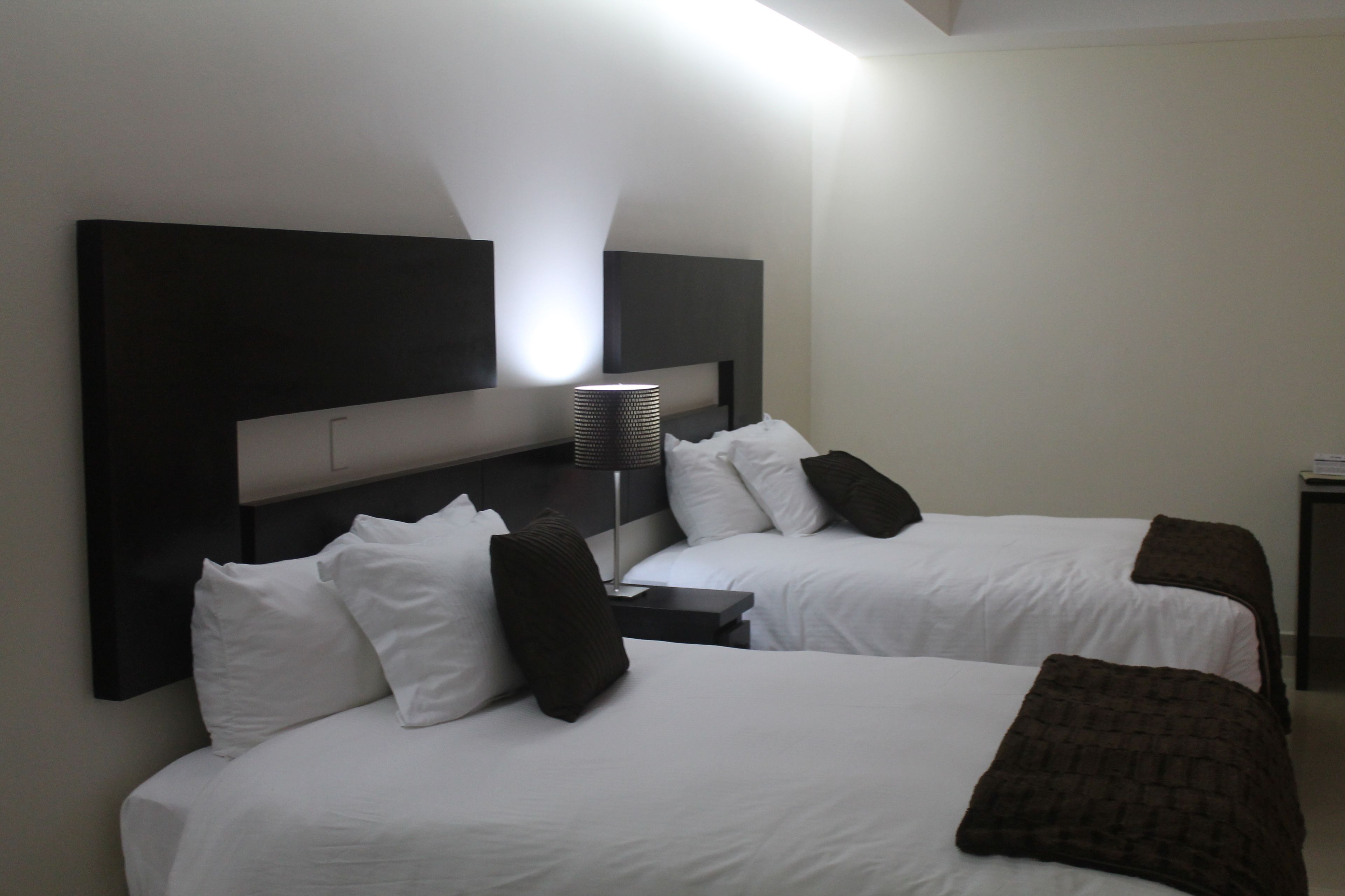 A hotel room with two beds, a headboard, a bedside table, and a lamp.