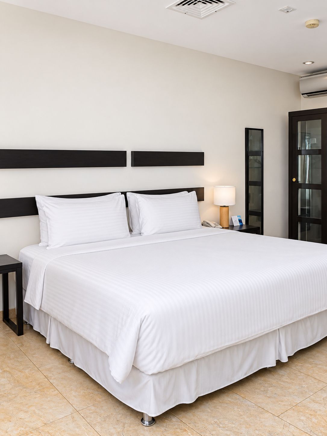 Una habitación de hotel con una cama grande, una mesita de noche, una lámpara y una puerta.