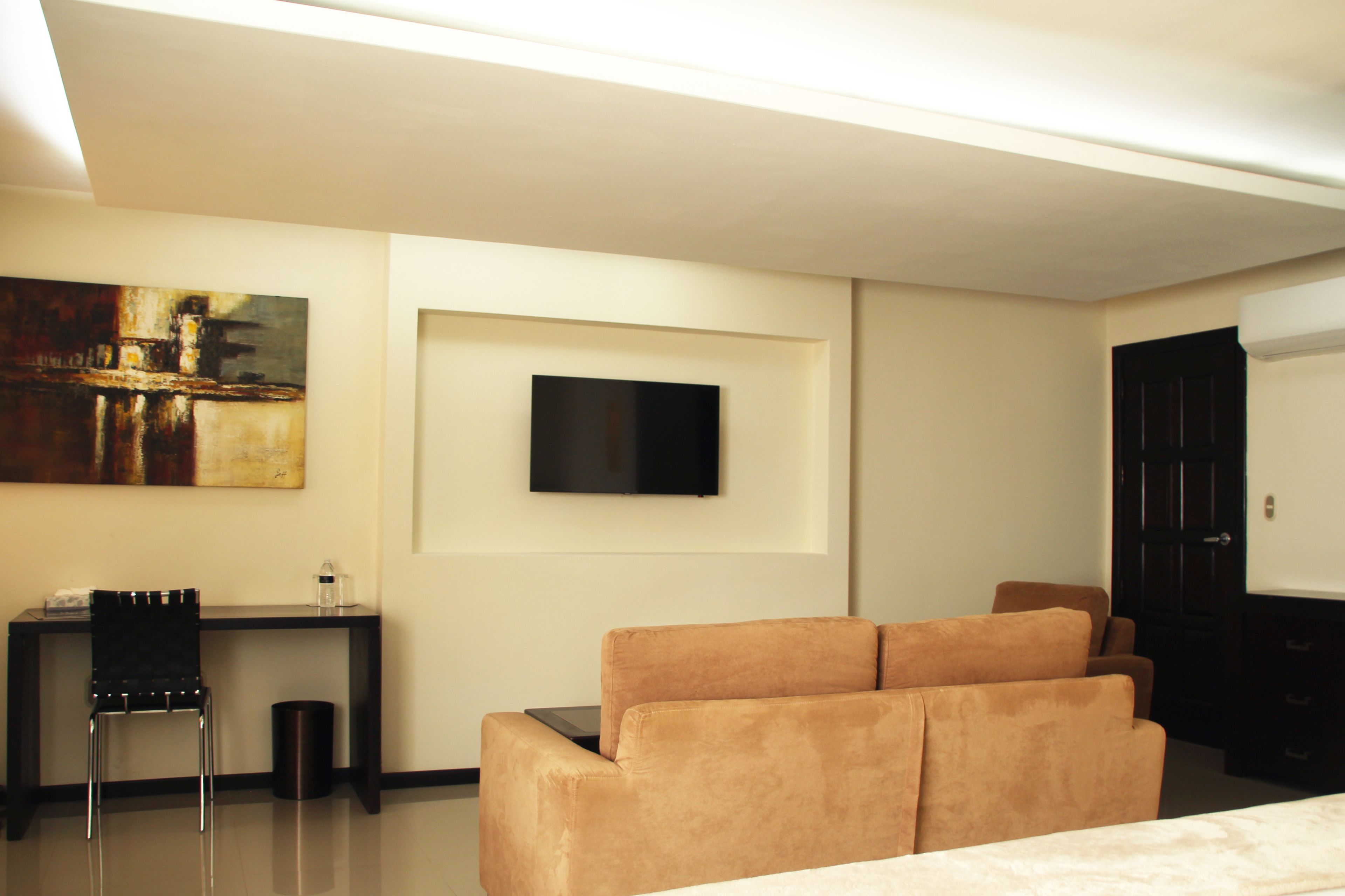 A modern hotel room with a sofa, a desk with a chair, a flat-screen TV, and a painting on the wall.