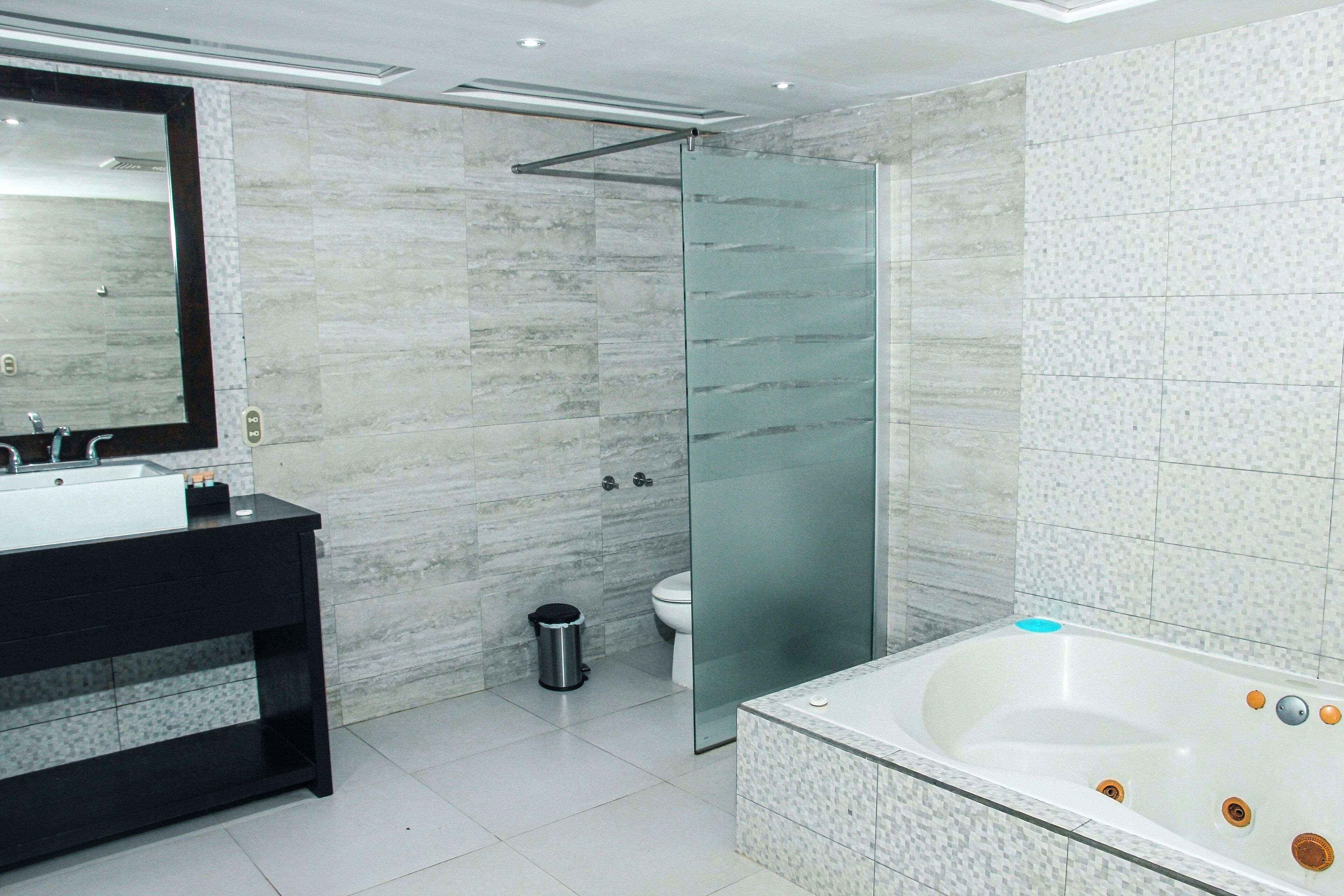A modern bathroom with a large mirror, a black vanity, a glass shower enclosure, and a freestanding bathtub.