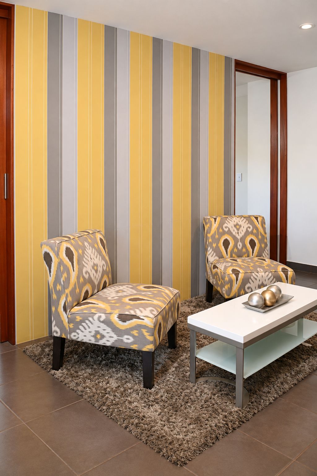 Una habitación con dos sillones estampados, una mesa blanca y una pared a rayas.