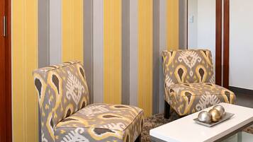 Una habitación con dos sillones estampados, una mesa blanca y una pared a rayas.
