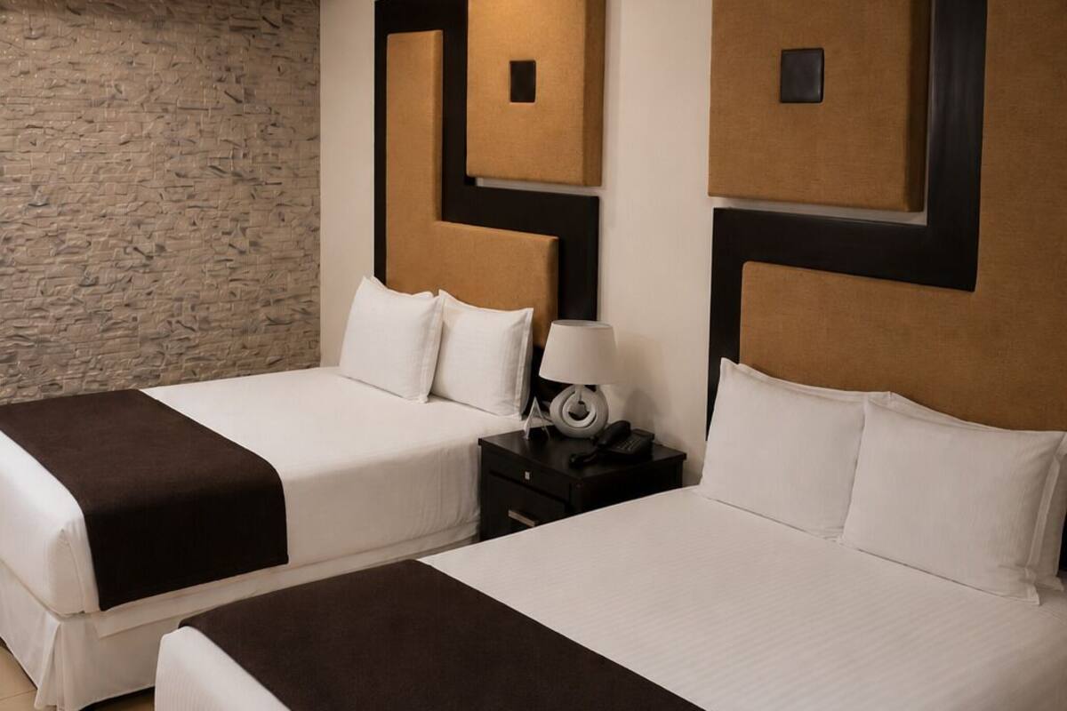 Two double beds with brown headboards and white bedding, a stone wall, and a nightstand with a lamp and phone.
