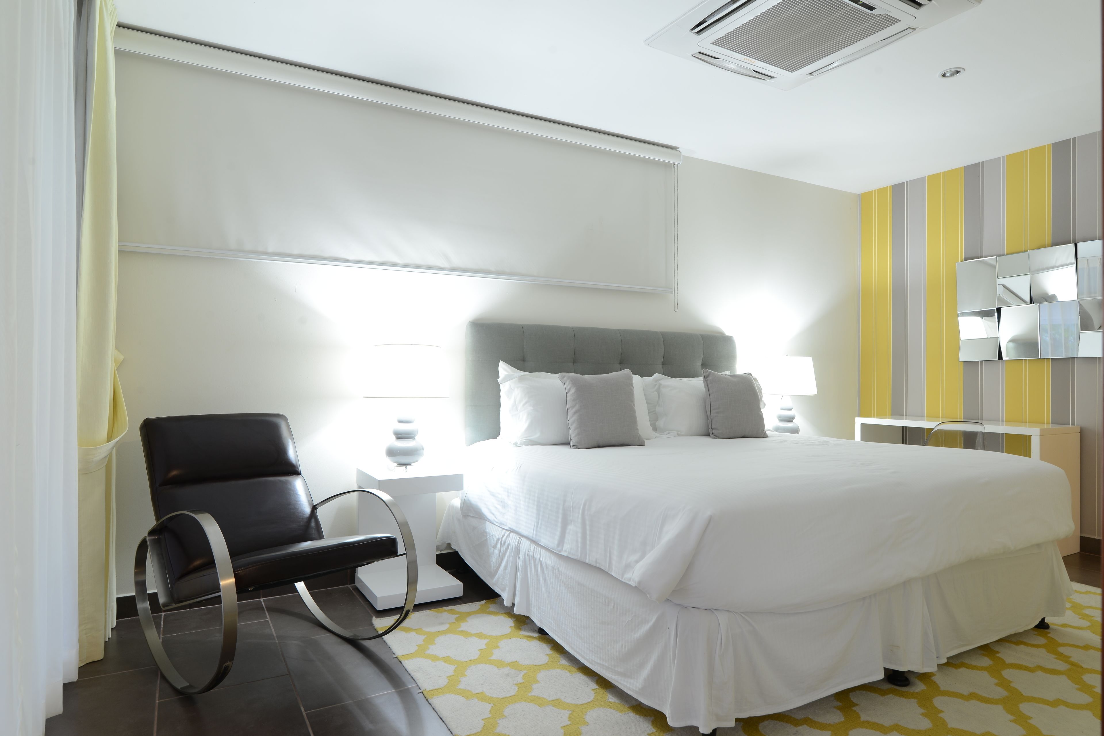 A modern hotel room with a large bed, a black chair, a bedside table, and a mirror on the wall.