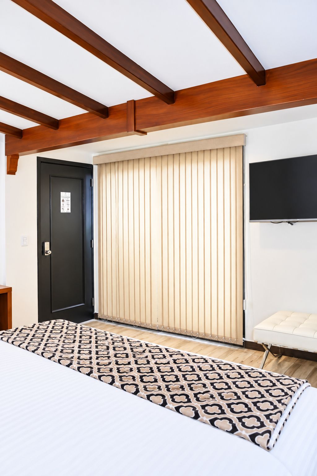 A bedroom with a bed, a black door, a sliding wooden door, a television, and a patterned rug.