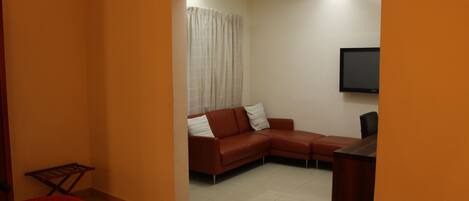 A room with a brown sofa, a TV mounted on the wall, and a red carpet.