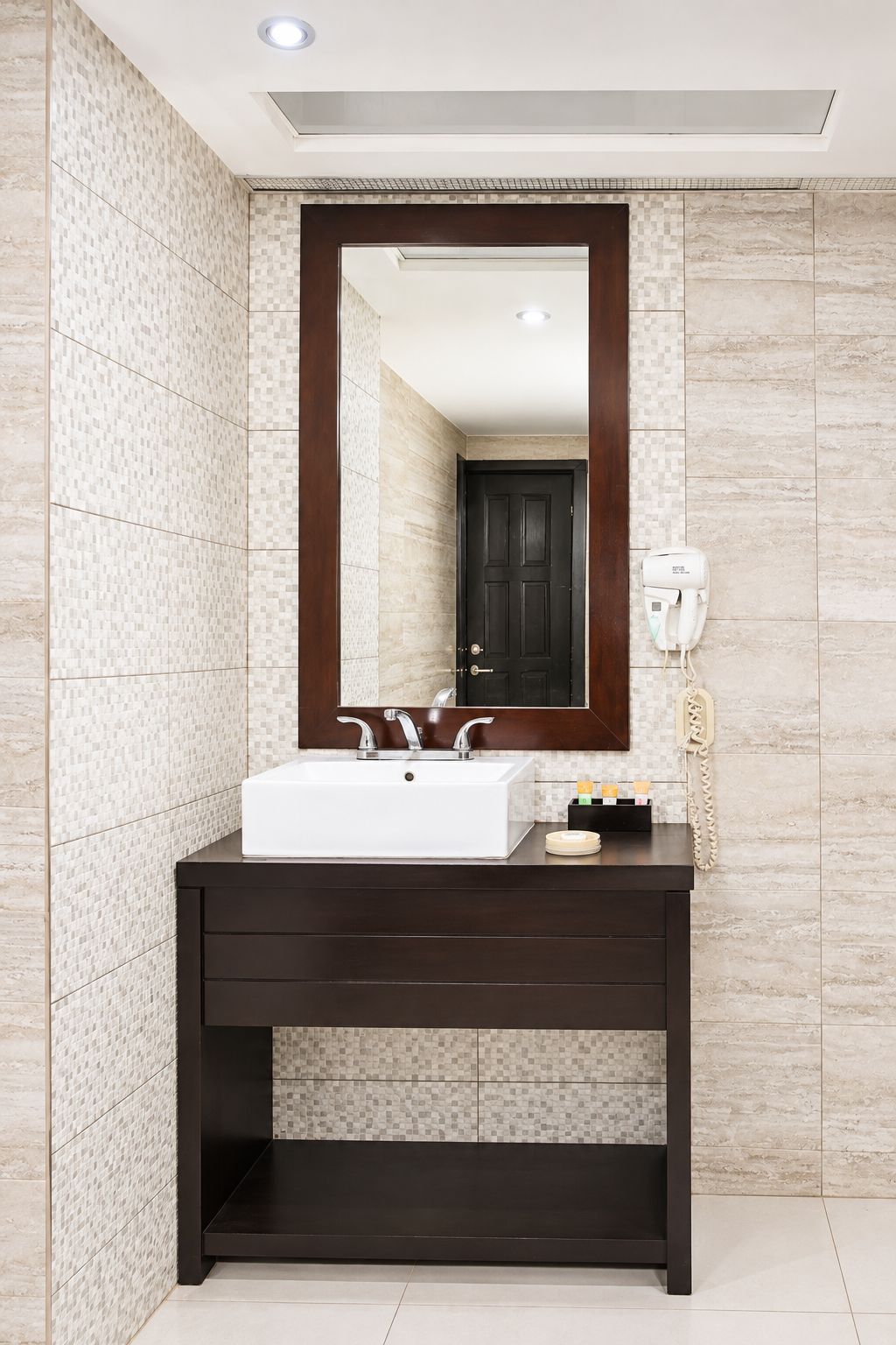 A bathroom with a white sink, dark vanity, tiled walls, and a mirror.