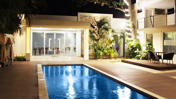 Ein Schwimmbecken mit Glasveranda, umgeben von einer Holzterrasse und einer Sitzgruppe im Freien.
