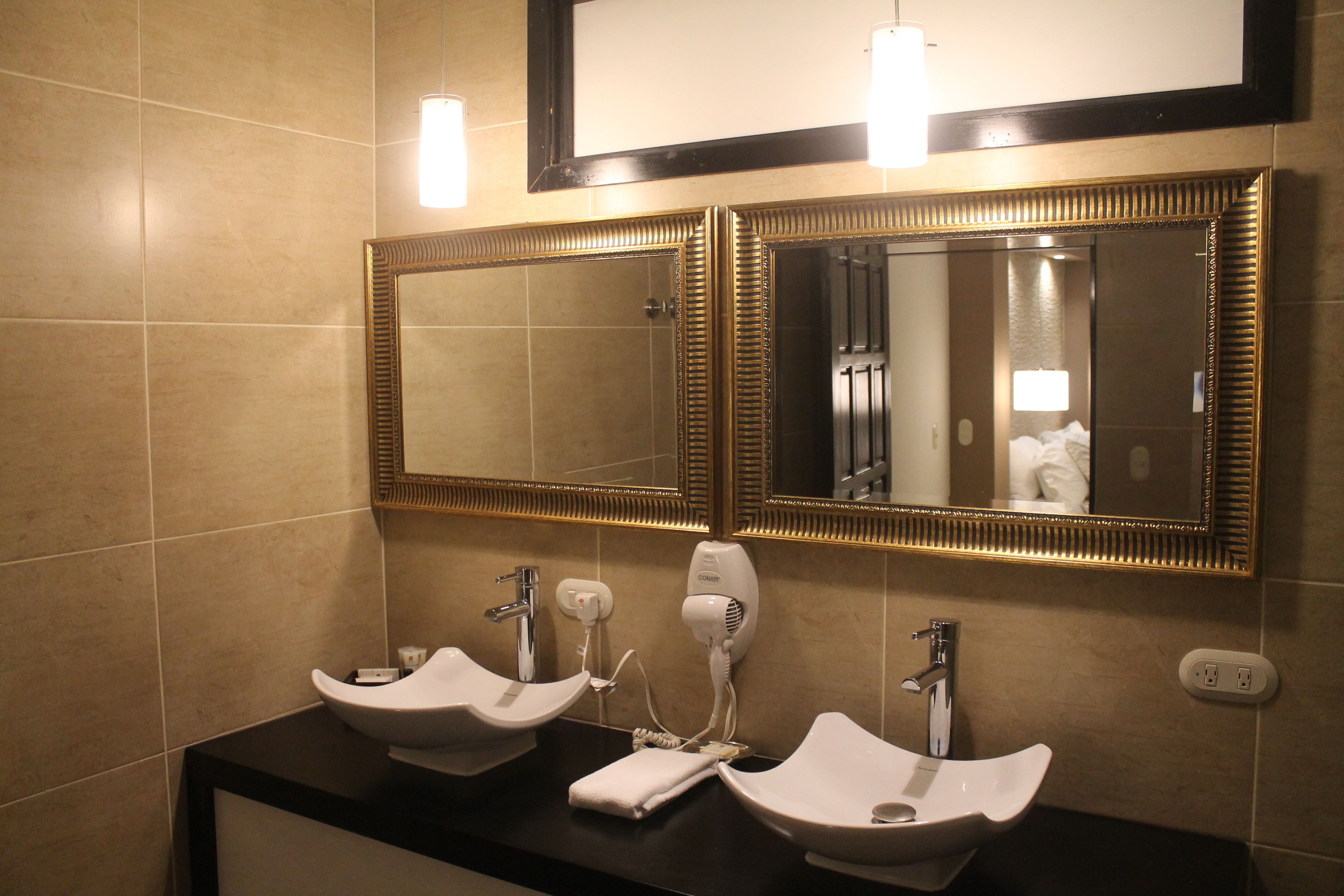 A bathroom with two sinks, a hairdryer, and a mirror with a gold frame.