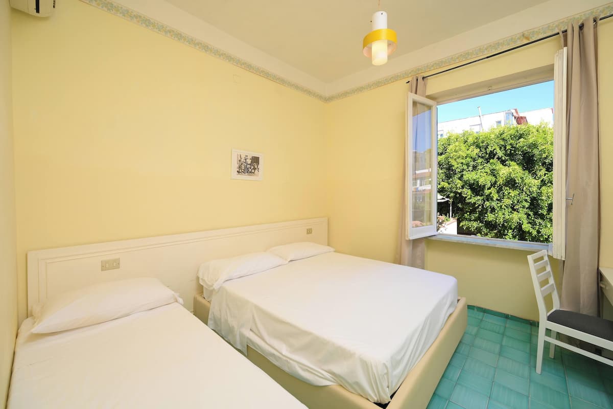 A room with two beds, a window with curtains, a chair, and a small table.