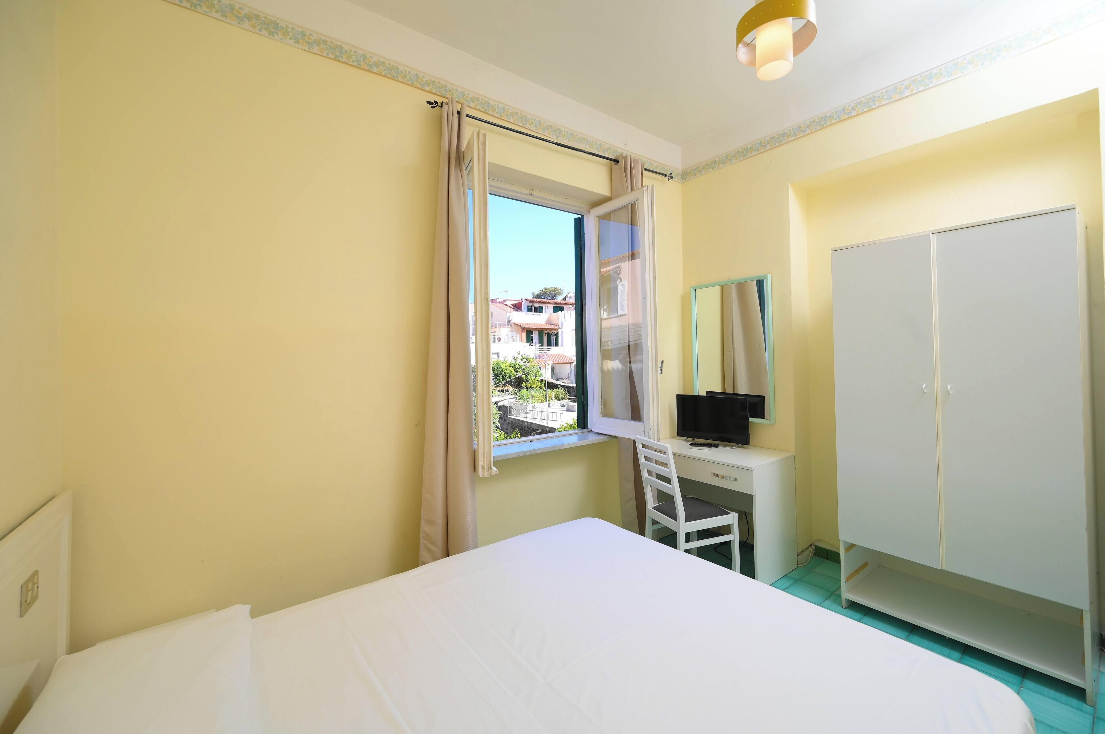 Een hotelkamer met een bed, een bureau met stoel, een kledingkast en een raam met gordijnen.
