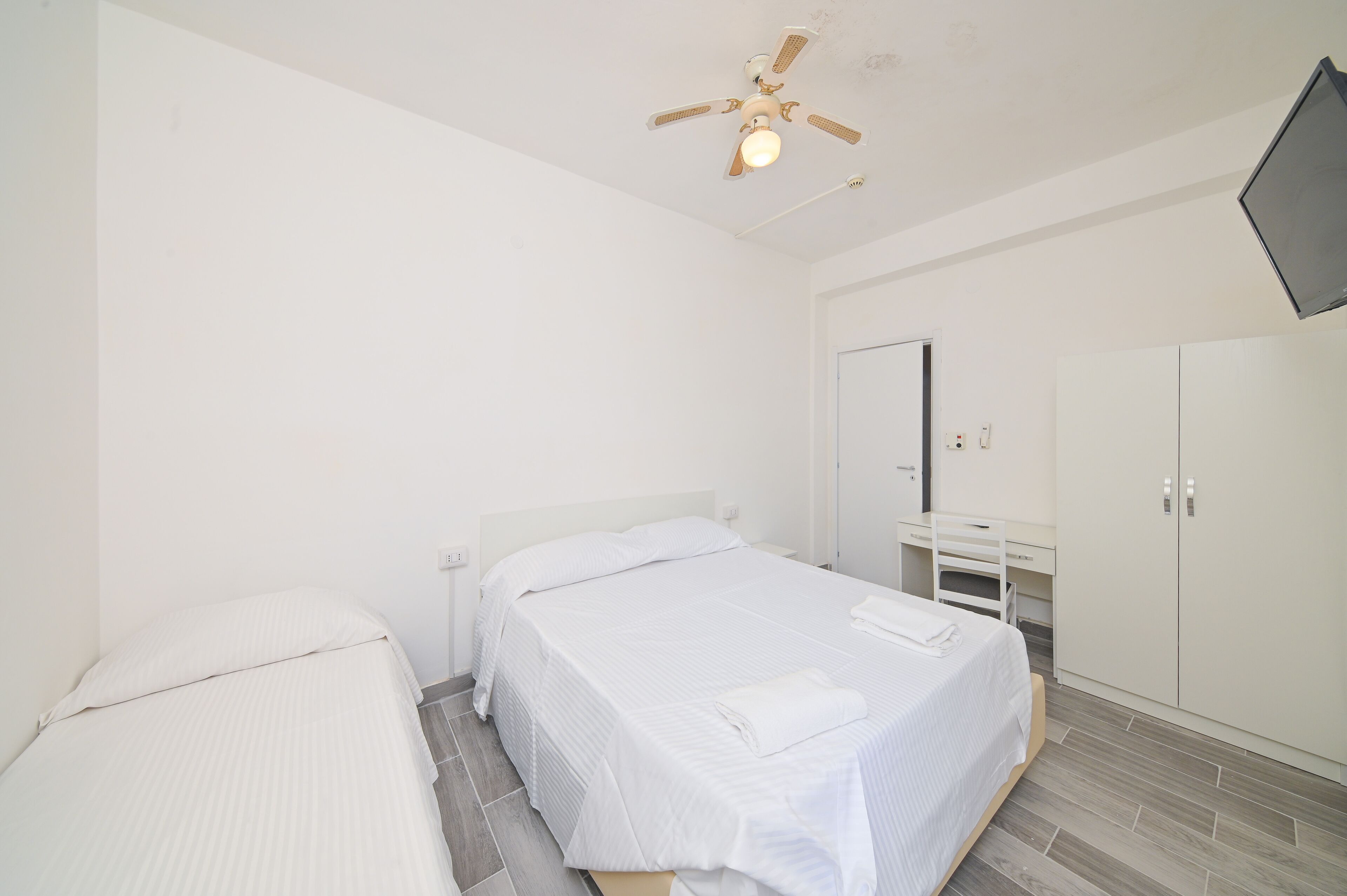 A bedroom with a bed, a desk, a wardrobe, and a ceiling fan.