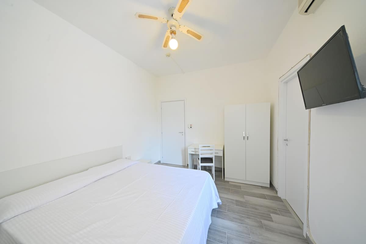 A bedroom with a bed, a desk, a wardrobe, and a ceiling fan.
