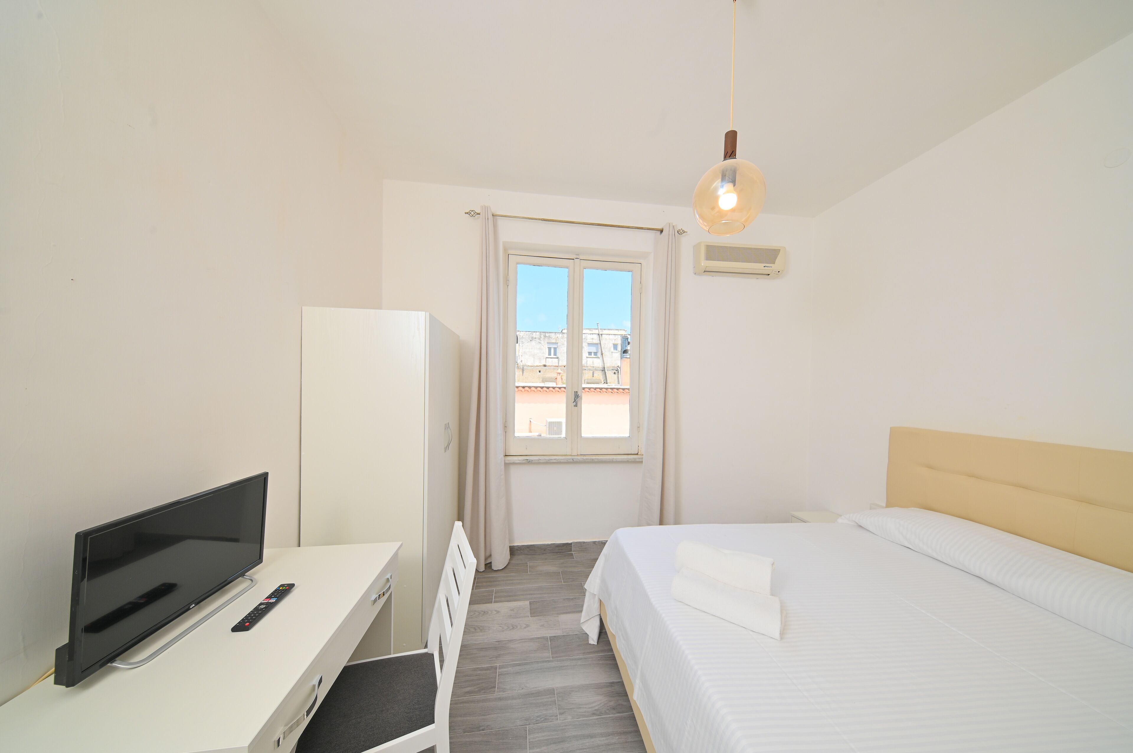 A hotel room with a bed, a TV, a desk, and a window with curtains.