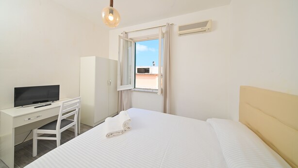 A hotel room with a bed, a desk with a television, a window with curtains, and a ceiling light. - Hotel Villa Diana (Ischia)