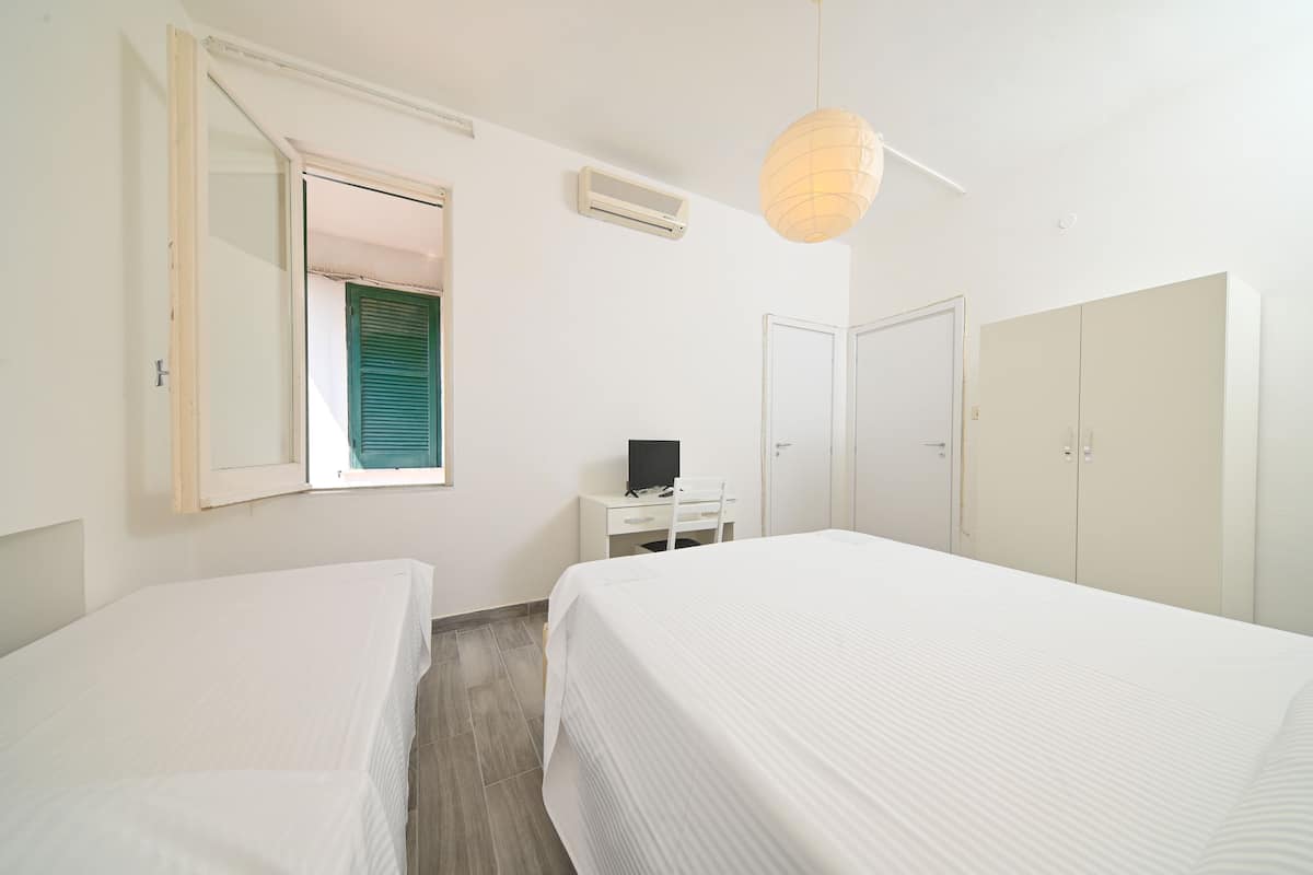 A hotel room with two beds, a desk with a computer, a wardrobe, and a window with blinds.