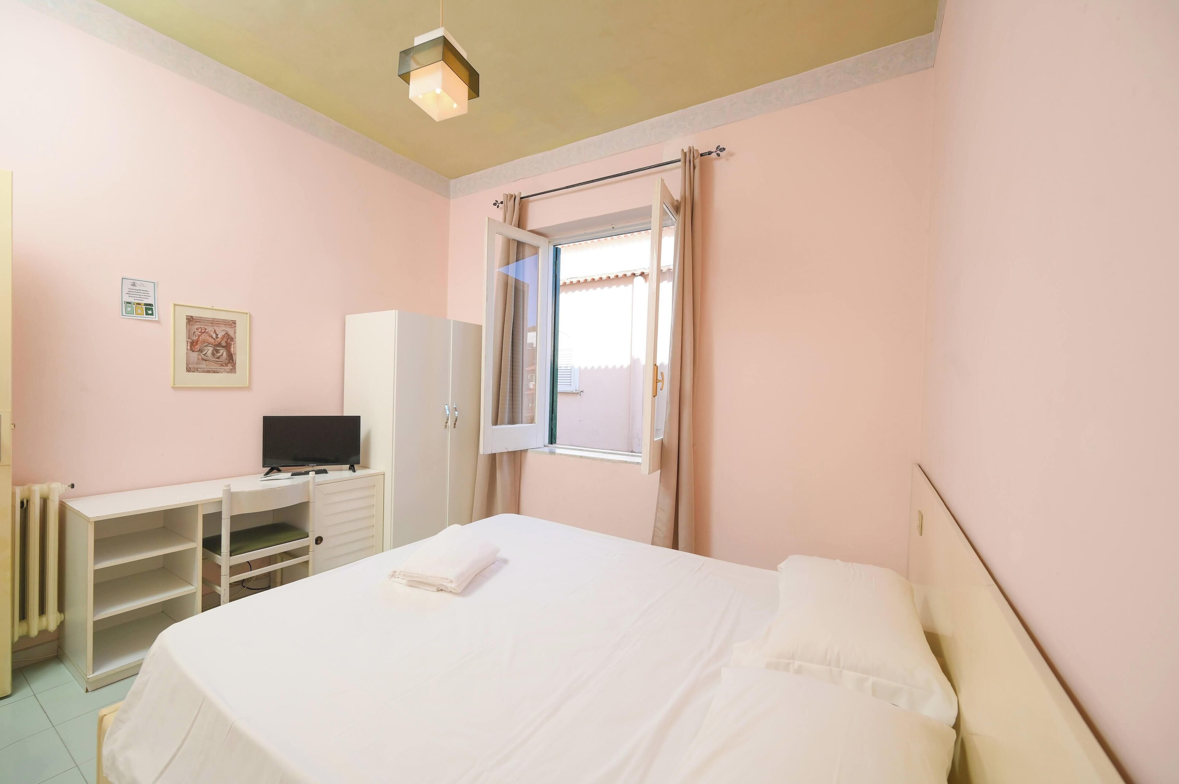 Un dormitorio con cama, televisor, armario y ventana con cortinas.
