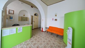 A reception area with a green counter, a bench, and a wall-mounted sign. - Hotel Villa Diana (Ischia)