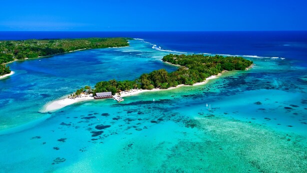An aerial view of a tropical island with clear turquoise waters, a small beach, and dense greenery.