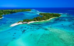 An aerial view of a tropical island with clear turquoise waters, a small beach, and dense greenery.