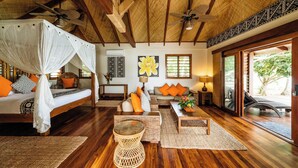 A spacious room with a wooden ceiling, a bed with a canopy, a sofa with orange cushions, and a large window offering a view of greenery.