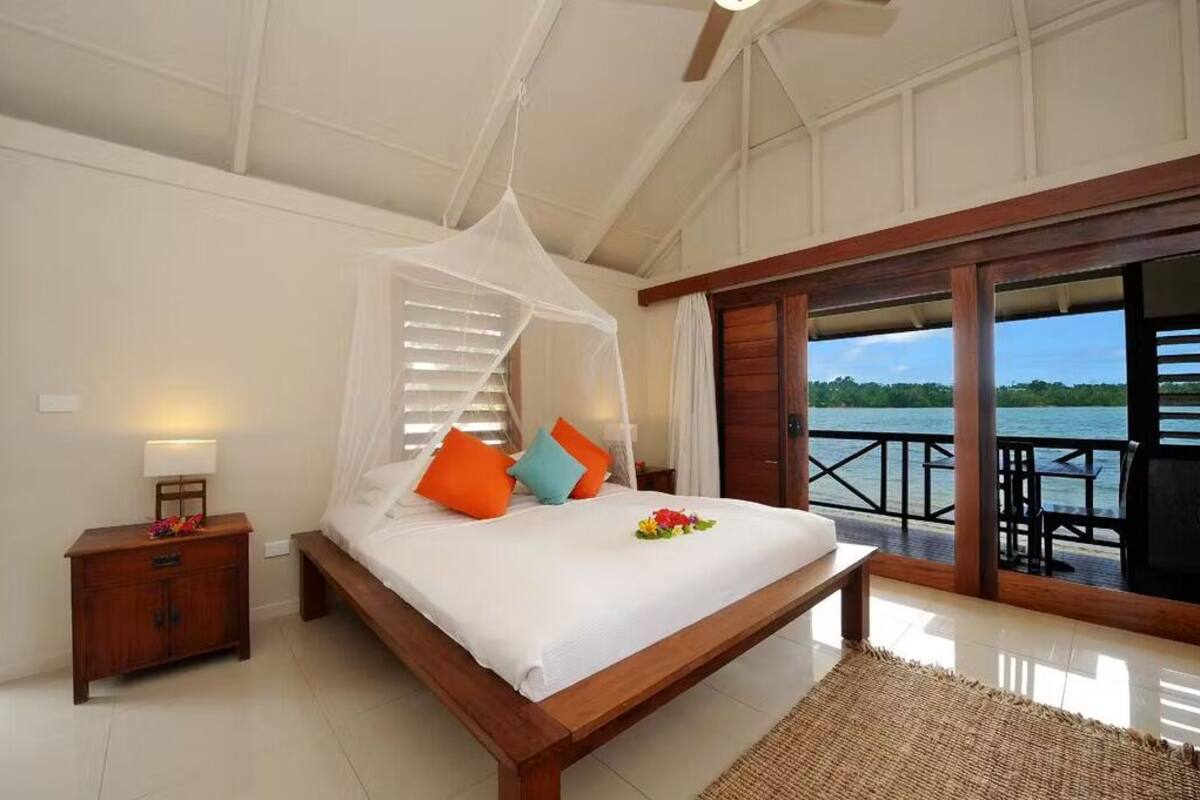 Een slaapkamer met een bed, nachtkastje en uitzicht op het water.