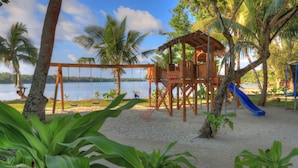 A beach playground with swings, a slide, and a wooden playhouse.