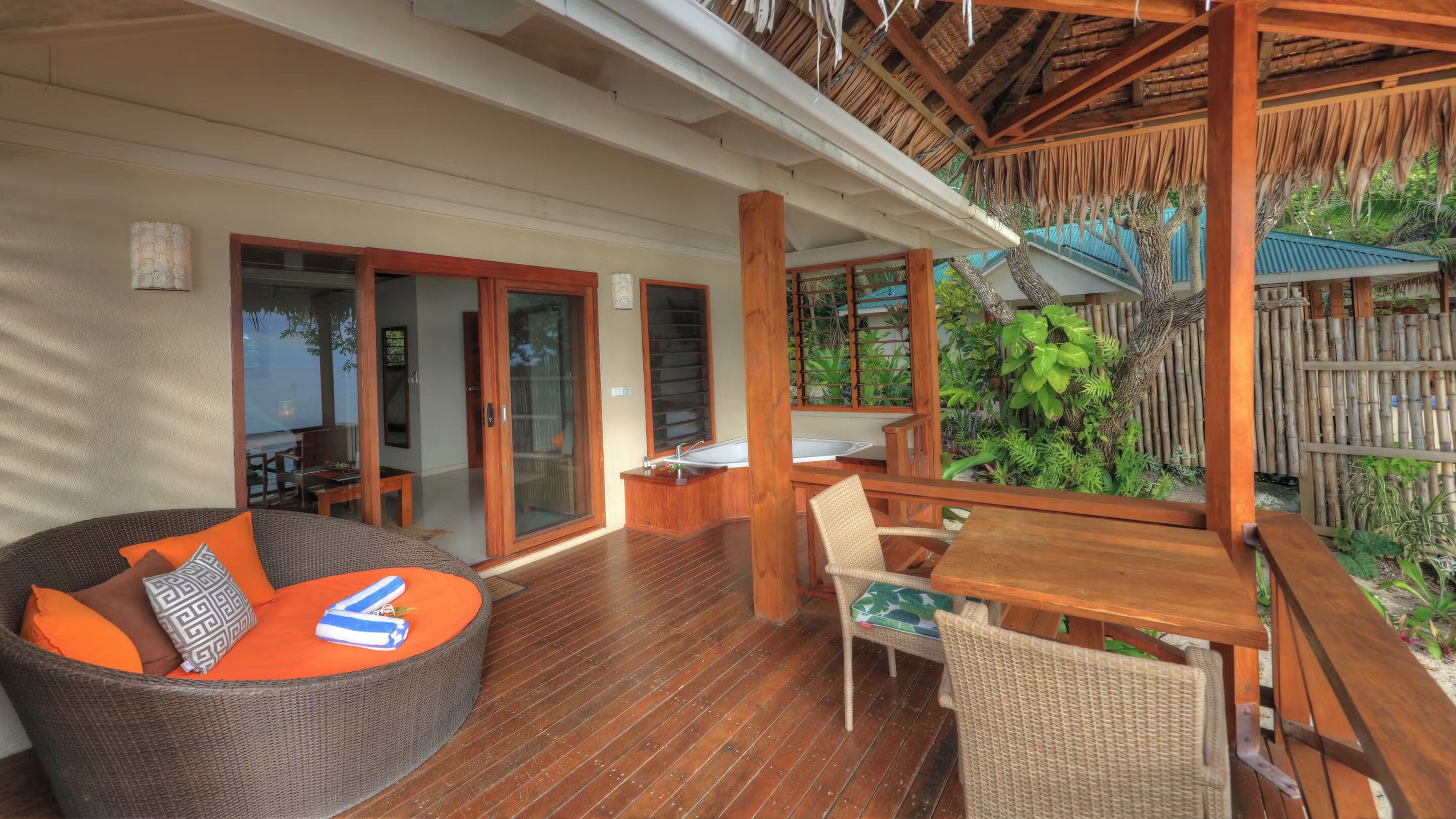 A wooden deck with wicker furniture, a wooden table, and a glass-enclosed sliding door leading to a patio area.