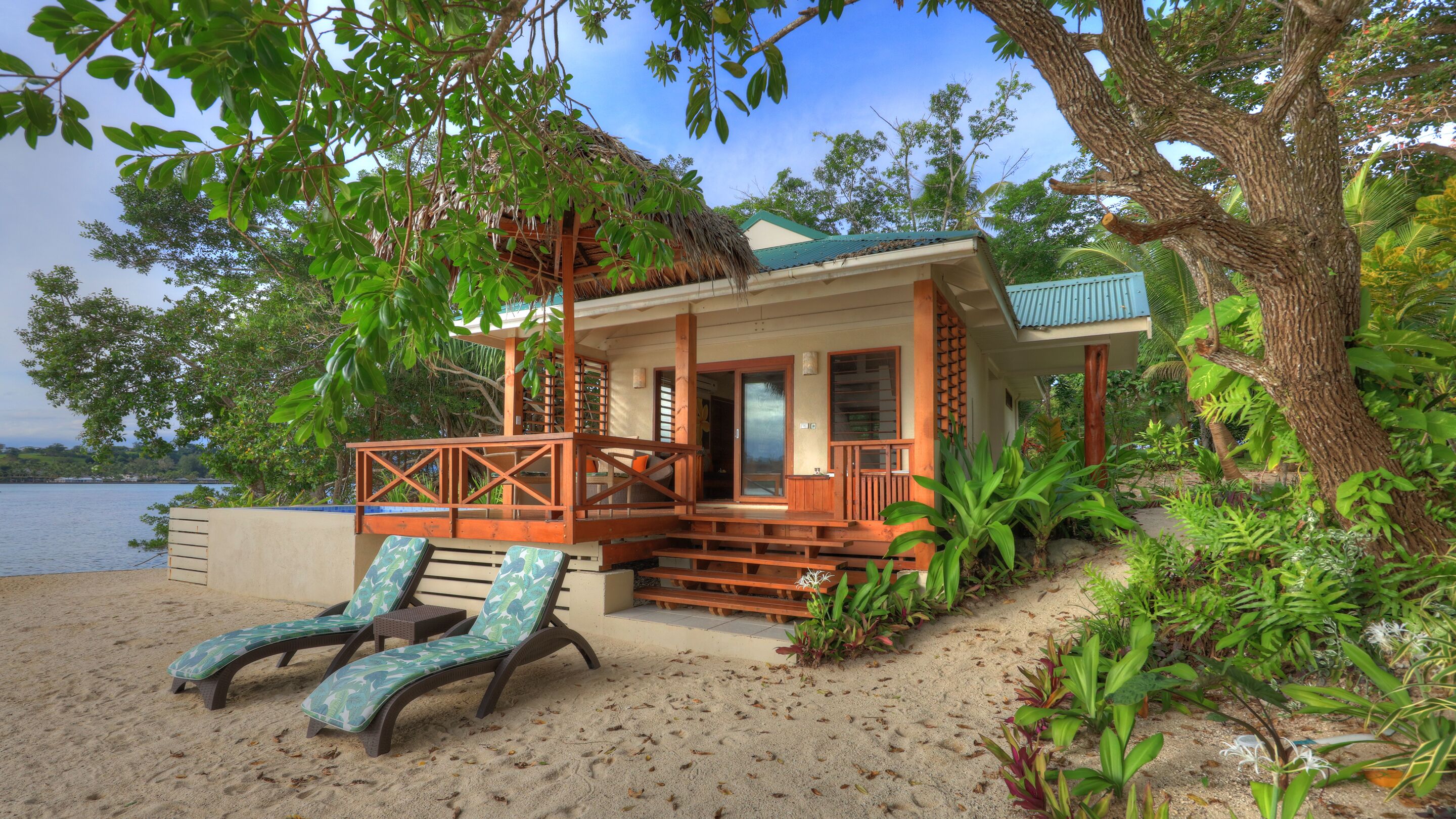 Een strandbungalow met een houten veranda, twee comfortstoelen en uitzicht op zee.