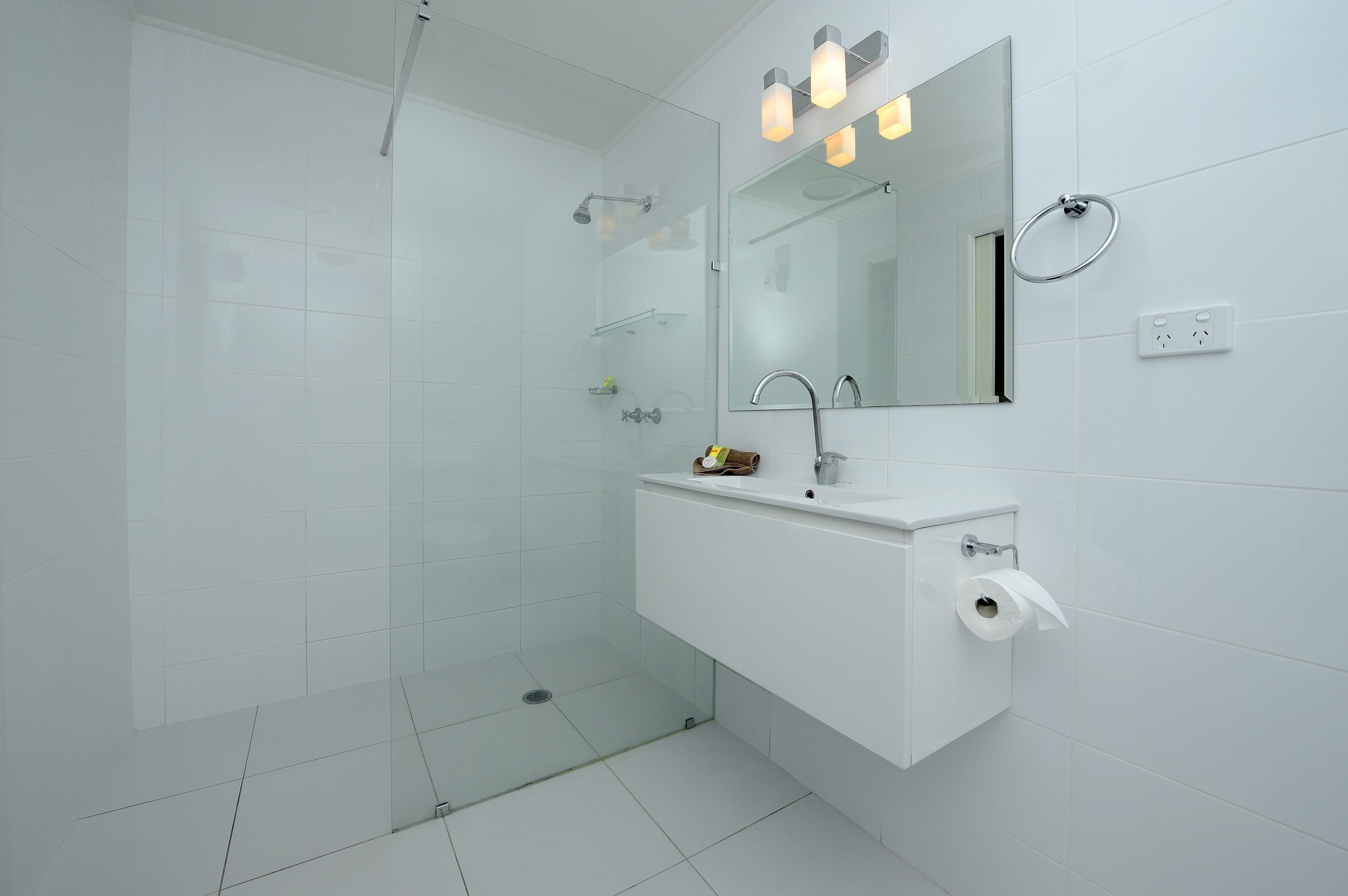 A modern bathroom with a glass shower enclosure, a white sink, and a mirror with lights above it.