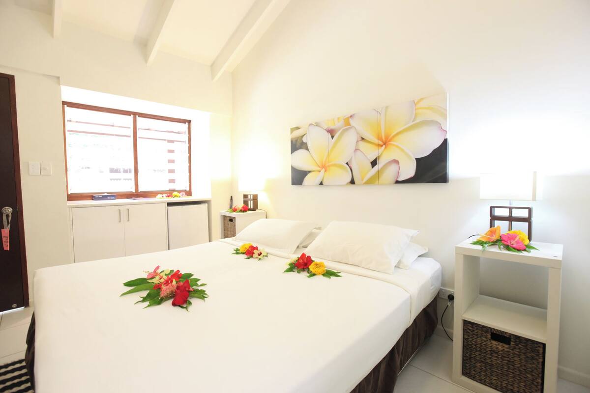 Een hotelkamer met een bed, een nachtkastje, een aan de muur hangend schilderij en een raam met jaloezieën.