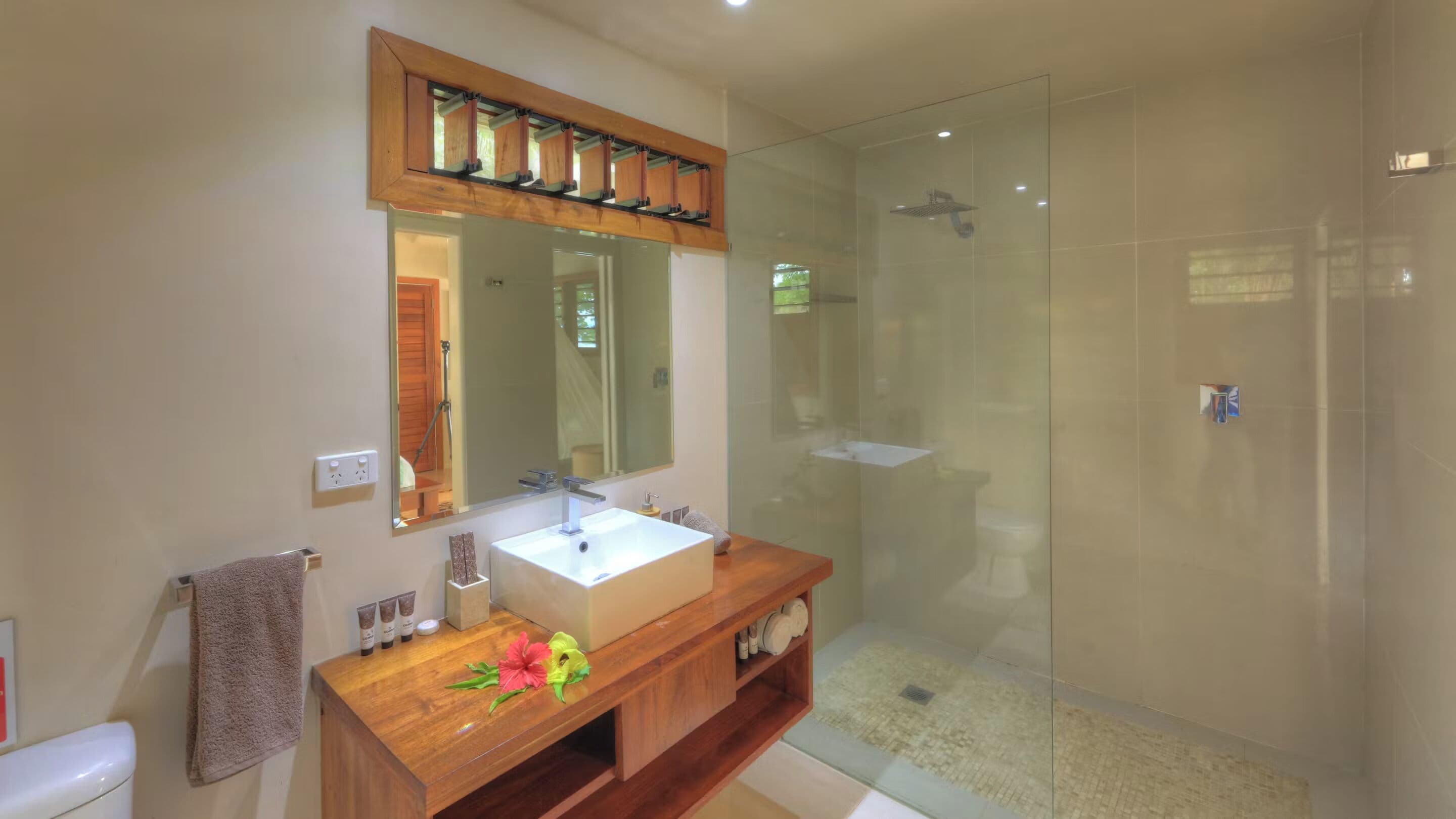 Un baño con tocador de madera, un espejo grande, cabina de ducha de vidrio y un inodoro.