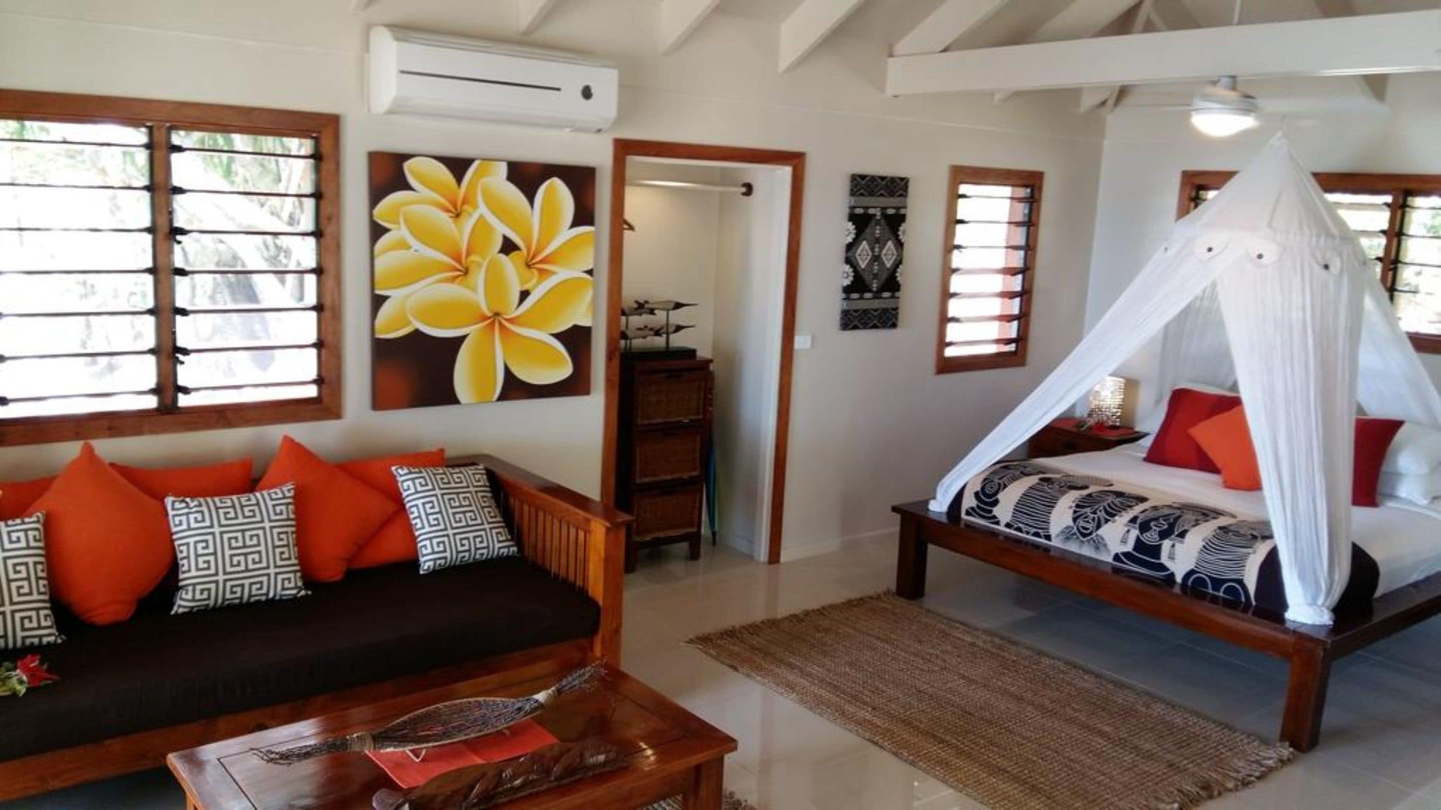 Una habitación con una cama bajo un dosel, un sofá con cojines estampados y una pared con un cuadro grande de flores.