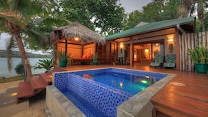 A poolside area with a thatched-roof structure, wooden deck, and a view of the sea.