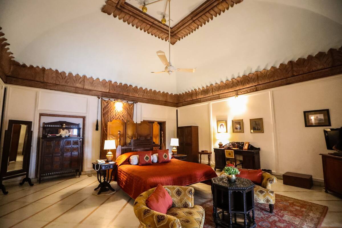 Ein geräumiges Schlafzimmer mit einem großen Bett, einer Sitzecke mit Sofa und Sesseln, einem Schreibtisch und einem Deckenventilator.