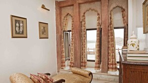 A room with a sofa, framed pictures on the wall, and a view through a window with curtains.