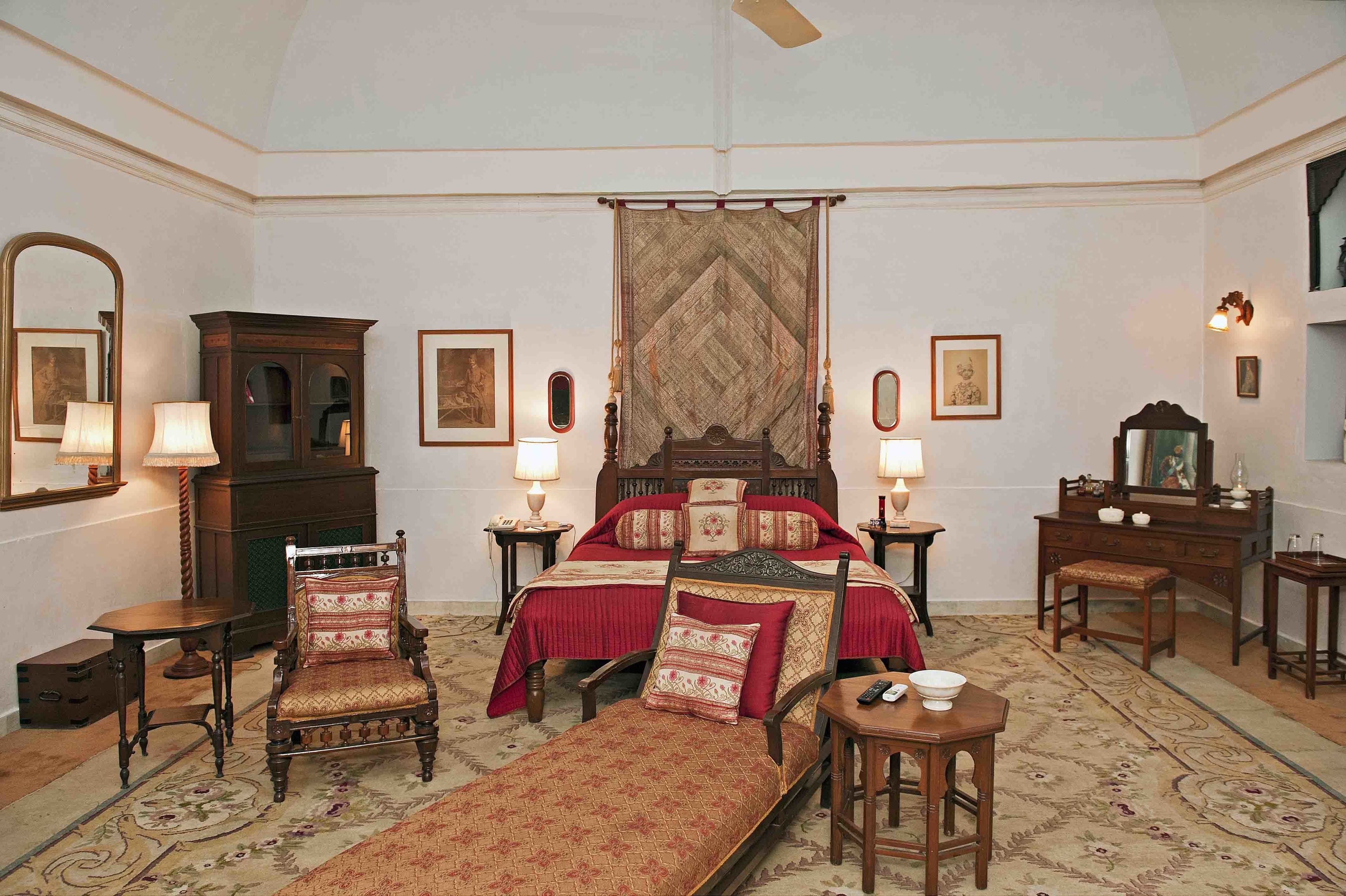 Een klassieke slaapkamer met een groot bed, twee nachtkastjes met lampen, een houten dressoir, een spiegel en een kamerbreed tapijt met dessin.