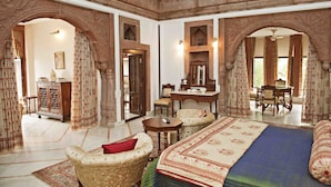 A traditional room with a bed, a desk, and two chairs. There are ornate arches and a large mirror.