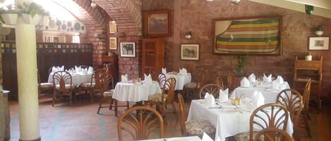 A restaurant with multiple tables set for dining, featuring wooden chairs and white tablecloths.